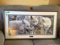 Framed print of three white wolves in natural setting inside wood-tone frame with white mat and glass, displayed on couch.