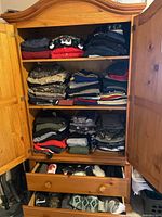 Full view of wooden armoire showing three shelves of folded garments and two drawers