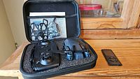 Open case containing the platinum drone, black controller, mesh pocket with accessories, and black 8GB Apple iPod Nano on wooden surface.