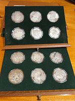 Overall view of wooden box open to show two velvet-lined drawers each holding six capsule-protected coins.