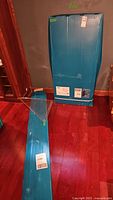 Two flat blue sealed cartons containing greenhouse panels and frame components on hardwood floor