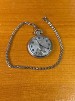 Overall view of pocket watch and chain laid out on surface