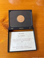 Coin in upper tray of presentation box with certificate visible below