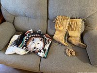 Photo showing two men's wildlife-themed shirts and two pairs of moccasin style boots including baby moccasins on couch