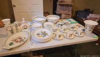 Full lot displayed on folding table showing plates, cups, bowls and serving pieces