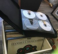 Photo of a milk crate filled with classical vinyl albums including Handel's Messiah, and the open zippered CD case showing multiple loose CDs without covers or jewel cases.
