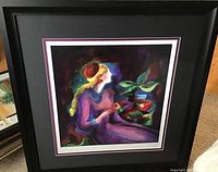 Framed artwork showing a woman in purple with a red beret sitting near a colorful plant, vibrant dark background.