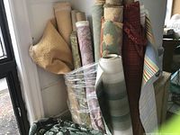 Display of multiple upholstery fabric bolts in varied patterns and colors including neutrals, florals, plaids, and stripes with fabric remnants visible.