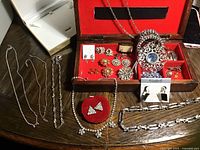 Overview photo of all jewellery items arranged around open red lined jewellery box showing most pieces in lot