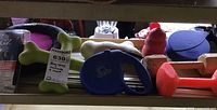 Shelf displaying assorted dog toys, chew toys including bone-shaped and dumbbell shapes, red Kong toy, and two blue retractable leashes.