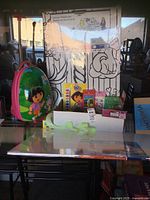 Photo of entire lot showing Dora the Explorer rolling suitcase, large coloring poster with animal cartoon designs, assorted stickers, coloring supplies, and foam board packaging.