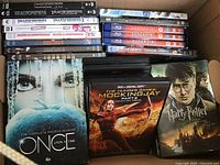 Photo showing a wide selection of DVDs including Once Upon a Time season 4, The Hunger Games, Harry Potter, and several other titles stacked in a box.
