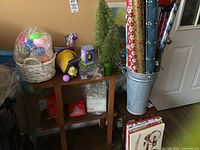 Photo showing Easter baskets with colorful plastic eggs, stuffed chick toy, sparkly Christmas trees, Christmas wrapping paper rolls, metal bucket for wrapping paper, and gift boxes beneath table.