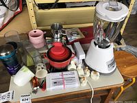 Photo showing assortment of kitchenware items including blender, coffee mugs, charcuterie board and others on a small table.