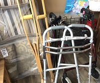 View of assembled walking aids including two walkers, wooden crutches, and two canes all arranged together.