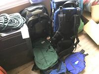 Four backpacks and a garden hose with lantern and camping gear in background on floor