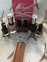 Six nail polish bottles including two large Sally Hansen Complete Salon Manicure bottles and four smaller bottles of various sparkly colors. Package of emery files placed in front.