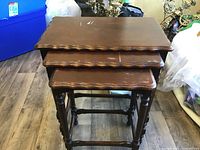 Stacked set of three wood nesting tables showing scalloped edges, wear and scratches on surfaces.