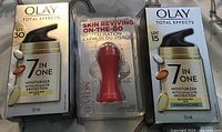Photo of two Olay Total Effects 7 in 1 moisturizers and one Revlon Skin Reviving roller on a patterned background.