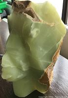 Front view of green stone sculpture showing face carving and natural rough edges with crystalline cavity.