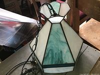 Image showing stained glass light fixture with white and green panels and black metal frame, with plug and chain attached.