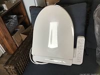 White Toto electronic bidet toilet seat with lid closed and control panel visible on right side, placed on a chair.