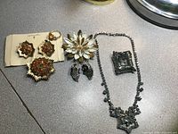 Overview of vintage signed costume jewelry: starburst rhinestone brooch and earrings, floral brooch, yellow stone ring, black rhinestone pendant and necklace.