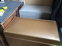 Two vintage brown vinyl ottoman storage boxes, one closed in front, one closed in back, placed in room corner.