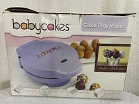 Front of the Babycakes Cake Pop Maker box showing the purple appliance and cake pops made with it.