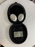 Open headphones placed inside the black carrying case showing the Bose logo on ear cups and the interior of the case.