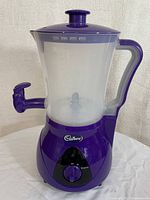 Purple and transparent electric hot chocolate maker with handle and tap dispenser, Cadbury logo visible, on a white surface.
