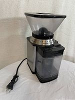 Side view showing the adjustable grind size dial on the clear plastic hopper and the grind container below with a stainless steel body.