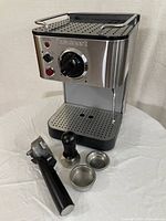 Front and side view of the Cuisinart espresso machine with portafilter, tamper, and two filter baskets placed in front.