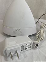 White essential oil diffuser with 1h, 2h, 3h timer buttons and ON button visible from front. Power cord connected but visibly damaged.