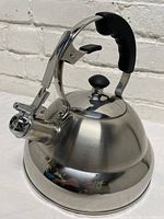 Side profile view of polished stainless steel kettle showing black handle, whistle spout cover, and brushed finish body.