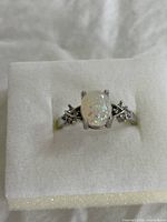 Front angle of sterling silver ring with synthetic pale opal and cubic zirconias on white cushioned background