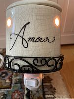 Front of ceramic night light on metal holder illuminated showing 'Amour' text and crackled glaze.