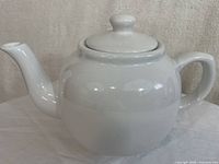 White ceramic teapot viewed from side showing spout, handle and lid.