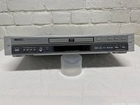 Front full view of the silver Toshiba DVD player model SD-3800SC on white surface with brick background