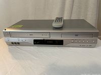 Front view of the Toshiba SD-V330 combo unit with remote on top, showing DVD and VCR slots and control buttons.