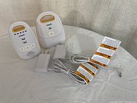 Two white and yellow VTech DM111 baby monitor units with power adapters on a white table.