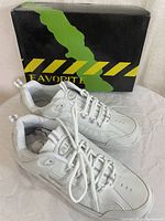 Pair of white running shoes with silver details and a box behind them, front side view.
