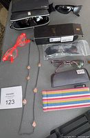 Various sunglasses and eyewear accessories including cases, necklace, and colorful eyewear strap.