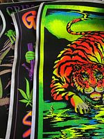 Photo showing details of three stacked black light velvet posters with visible neon colors including orange tiger and psychedelic graphics.