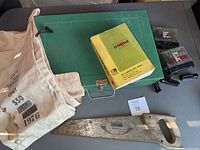 Overview of the lot including green metal toolbox, Dodge parts catalog, canvas bag, and saw