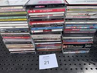 Stacks of multiple music CD jewel cases showing various artist names and titles in a zoomed-out view.