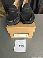 Front view of black suede womens Cole Haan Monroe Penny loafers sitting on their original box with a lot tag.