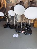Four black desk lamps arranged side by side, showing dome-shaped white diffused heads and round bases.