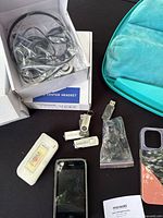 Photo of Wantek headsets (two opened sets, one sealed in box), original iPhone, USB flash drives, earphones, and phone case on black surface with a turquoise laptop pouch.