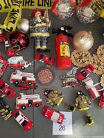Top-down view of assortment of fire station themed Christmas ornaments including miniature vehicles, figures, baubles, fire extinguisher, and firefighting tools.